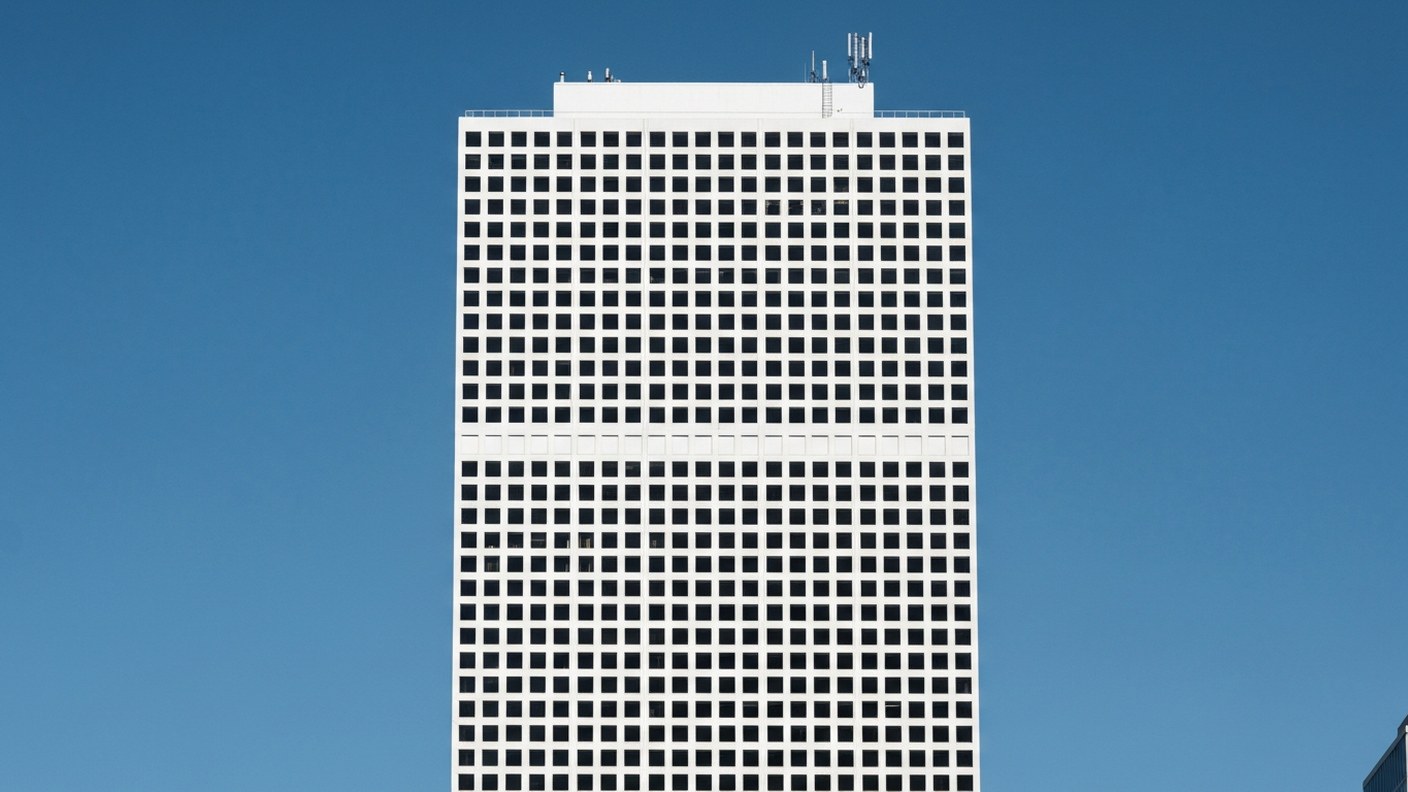 An extremely tall slender white concrete residential tower with a perfect grid of square windows ris