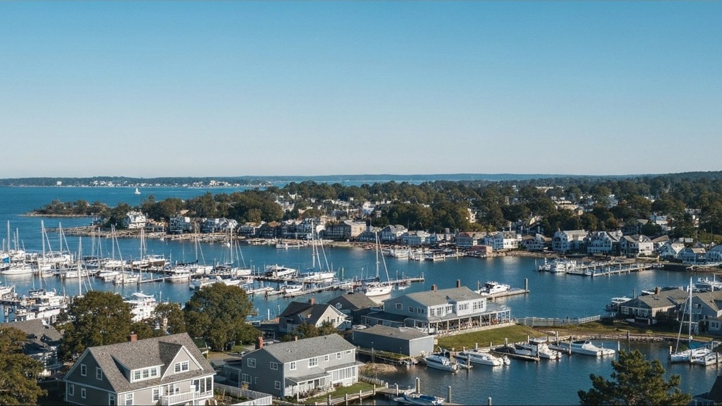 coastal town harbor with sailboats and waterfront homes, clear sky